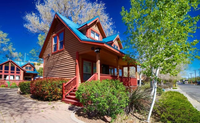 Red cottage-style house with turquoise roof, front porch, and landscaped yard on residential street